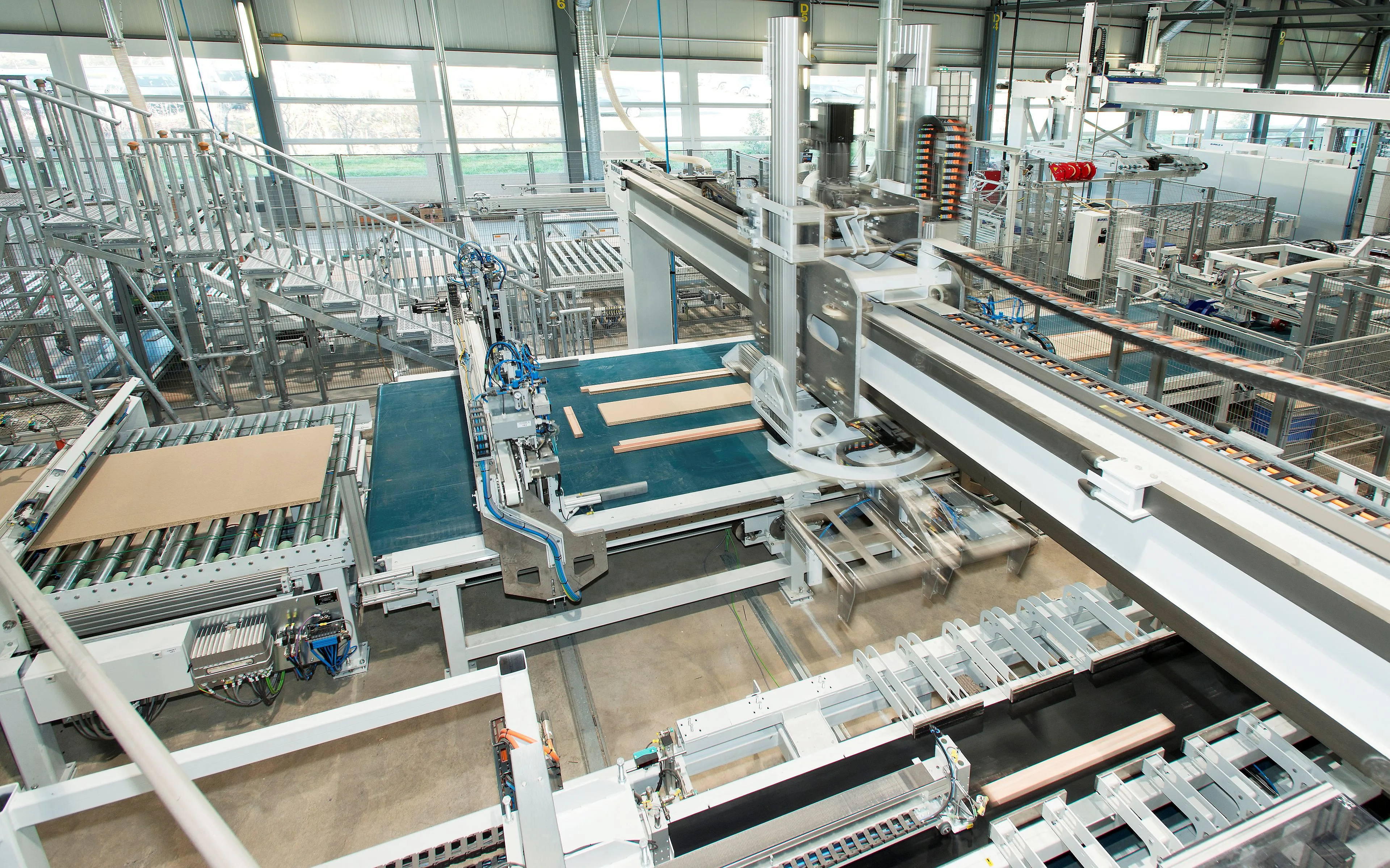 Blick in eine helle Produktionshalle mit Förderbändern und einer großen Roboter-Gantry, die Holzplatten als Türblätter verarbeitet und transportiert.