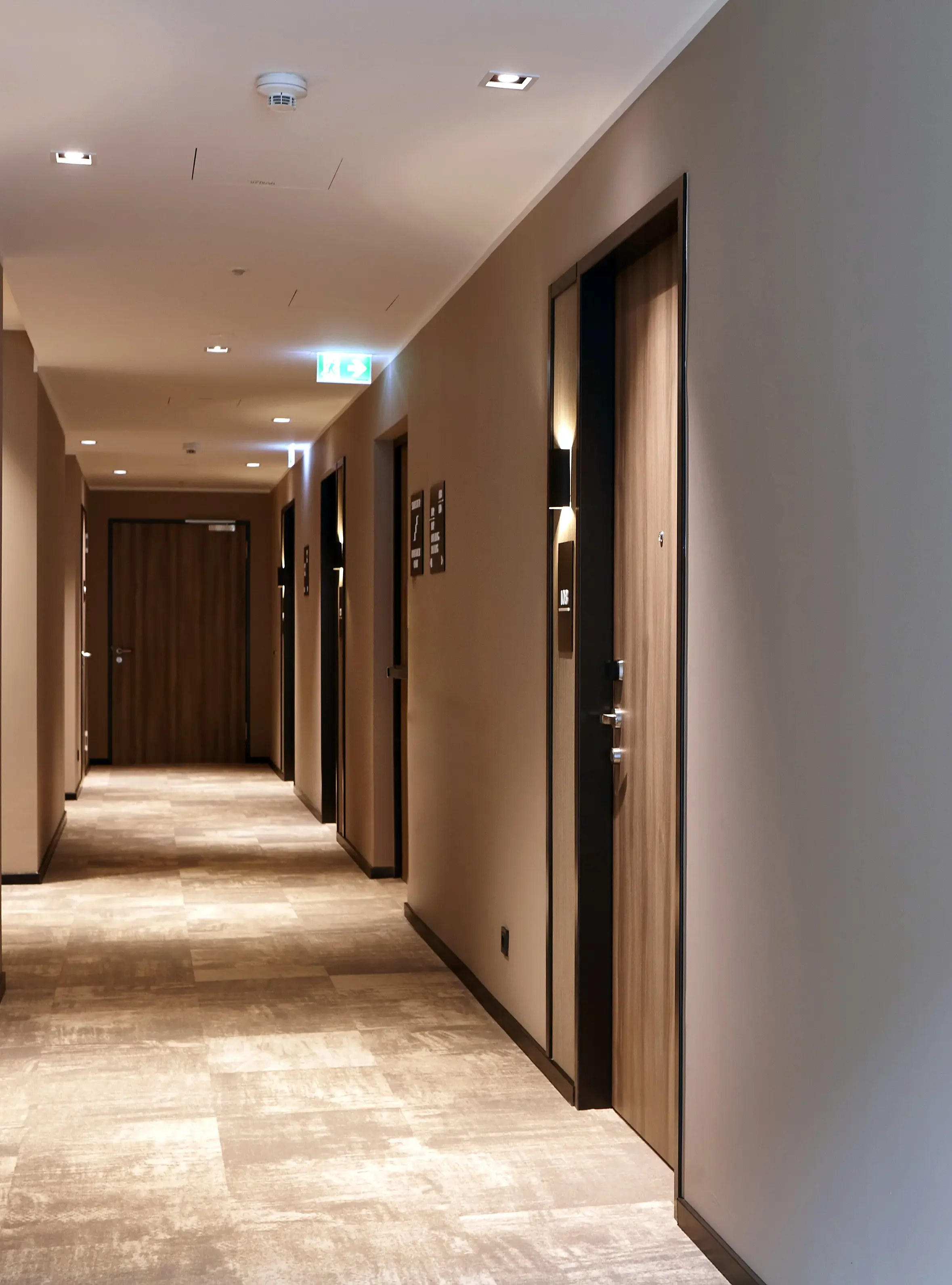 Viele Zimmertüren aus Holz in beleuchteten Hotelflur